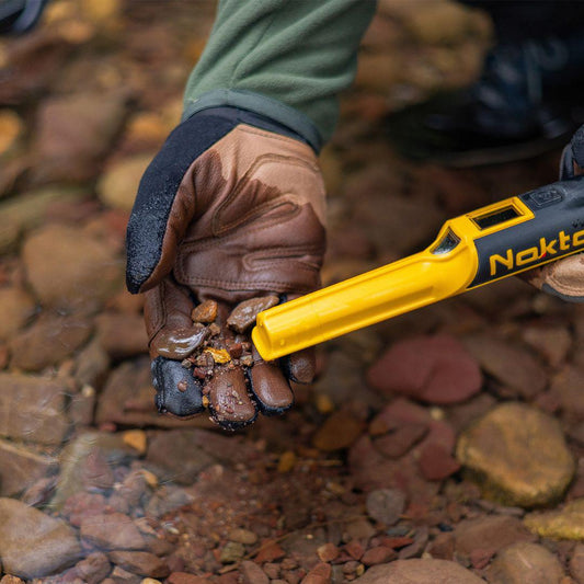 Original Nokta AccuPOINT pinpointer beside a gloved hand holding wet gravel during target recovery